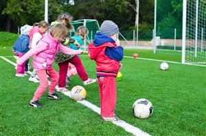 Young Kids Kicking Soccer Ball Into The Net During Practice