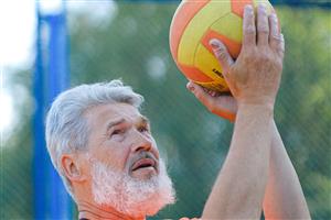 Senior man about to serve a yellow and orange volleyball